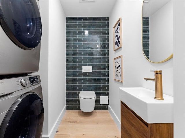 half bathroom featuring toilet, vanity, stacked washing maching and dryer, wood finished floors, and tile walls