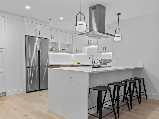 kitchen featuring a peninsula, light wood-style flooring, island exhaust hood, stainless steel refrigerator, and white cabinets