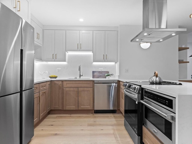 kitchen with light countertops, a peninsula, island range hood, stainless steel appliances, and a sink