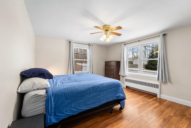 bedroom with radiator heating unit, multiple windows, baseboards, and wood-type flooring