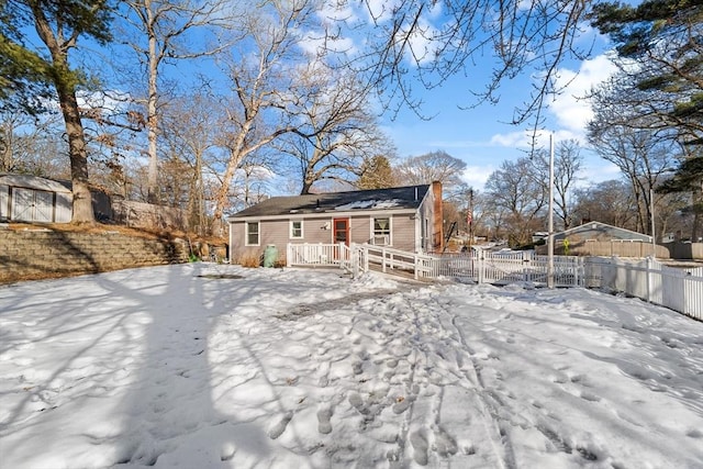 snow covered house featuring fence private yard, a storage shed, and an outbuilding