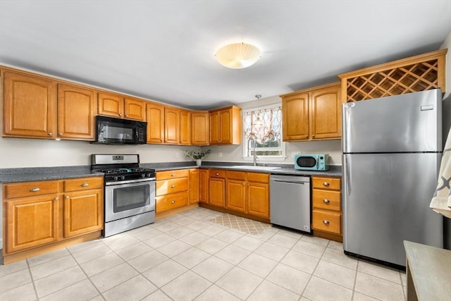 kitchen with brown cabinets, light tile patterned floors, stainless steel appliances, dark countertops, and a sink