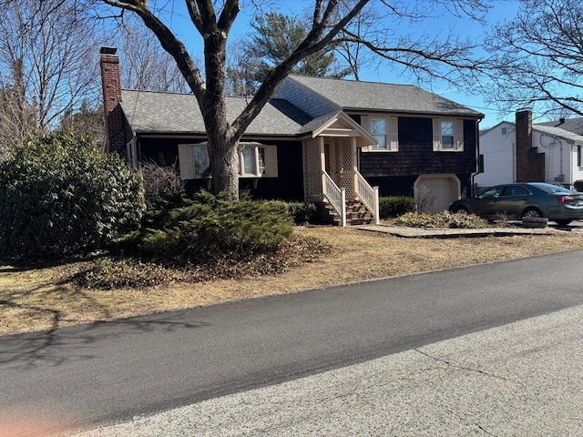 split level home featuring an attached garage, a chimney, and a shingled roof