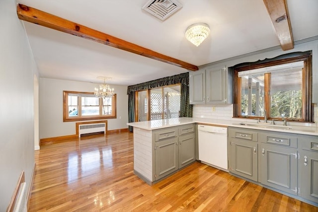 kitchen featuring visible vents, radiator heating unit, a peninsula, white dishwasher, and a chandelier