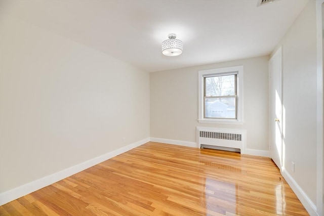 empty room featuring baseboards, radiator, and light wood-style flooring