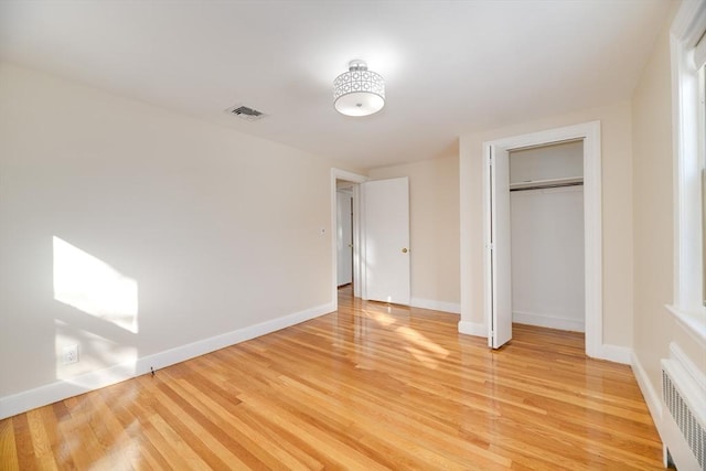 unfurnished bedroom with light wood finished floors, visible vents, radiator, baseboards, and a closet