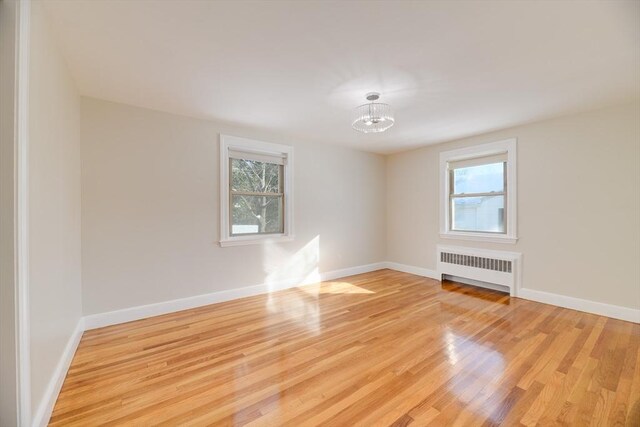 empty room featuring a notable chandelier, radiator heating unit, baseboards, and light wood-type flooring