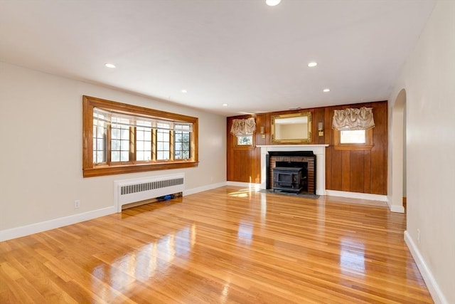 unfurnished living room with arched walkways, recessed lighting, light wood-style flooring, and radiator heating unit