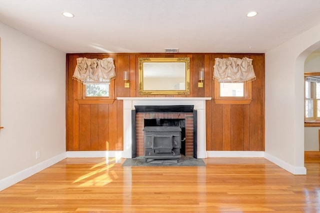 unfurnished living room featuring arched walkways, wood walls, baseboards, and wood finished floors