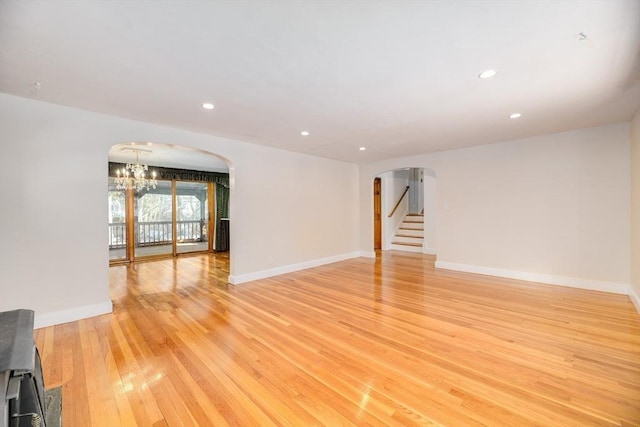 unfurnished living room featuring baseboards, arched walkways, light wood-style floors, and a notable chandelier