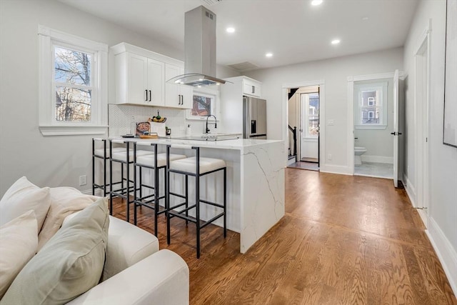 kitchen with white cabinets, a kitchen breakfast bar, stainless steel refrigerator with ice dispenser, light hardwood / wood-style floors, and island exhaust hood