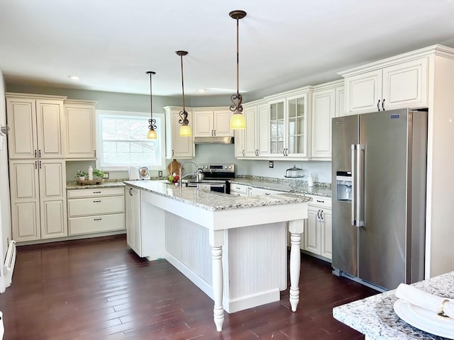 kitchen featuring glass insert cabinets, under cabinet range hood, hanging light fixtures, dark wood-type flooring, and appliances with stainless steel finishes