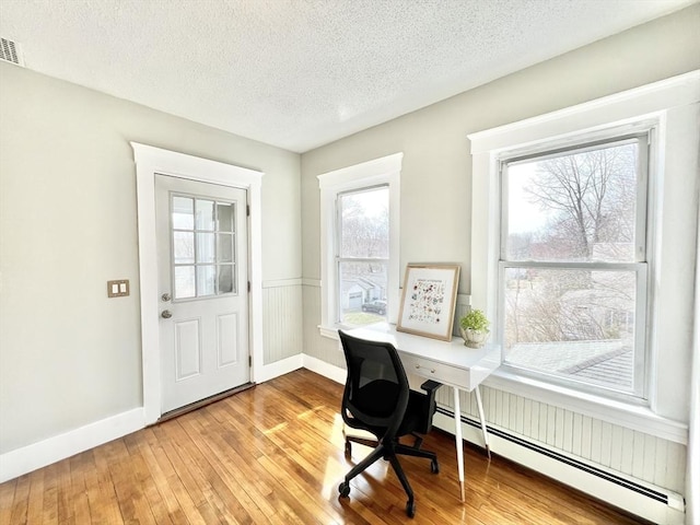 office featuring a textured ceiling, hardwood / wood-style floors, a baseboard radiator, and plenty of natural light