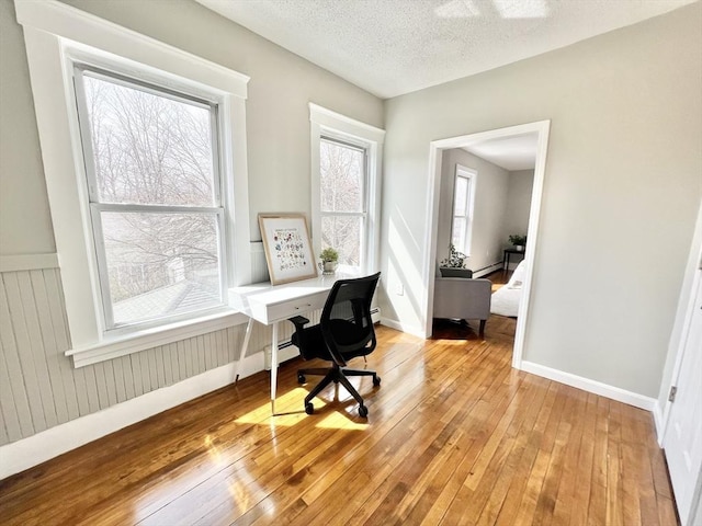 home office with a baseboard heating unit, a textured ceiling, wainscoting, baseboards, and light wood-style floors
