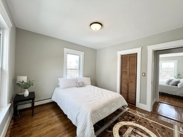 bedroom with a closet, dark wood-type flooring, baseboards, and a baseboard radiator