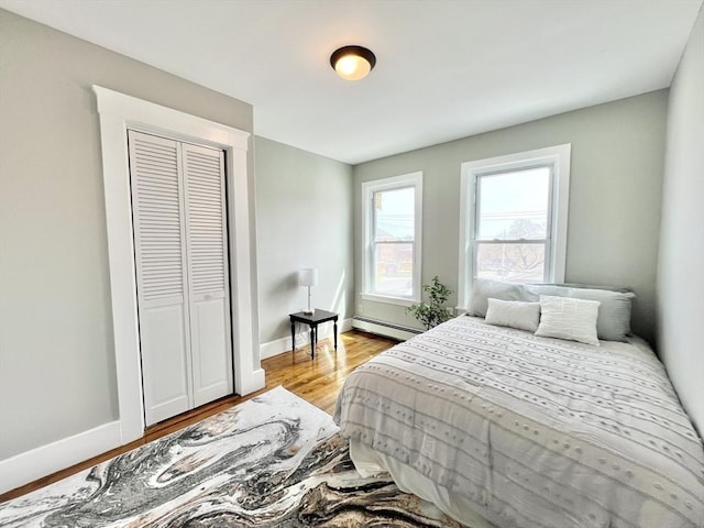 bedroom with a closet, light wood-style flooring, baseboards, and a baseboard heating unit