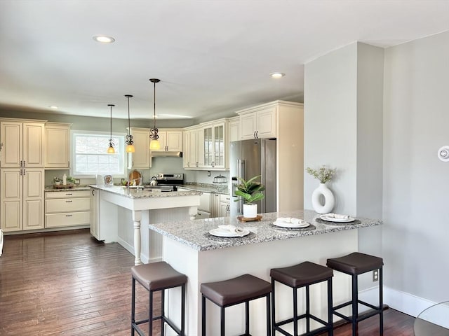 kitchen featuring a peninsula, a breakfast bar, recessed lighting, light stone countertops, and appliances with stainless steel finishes