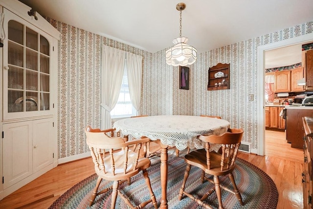 dining space with visible vents, light wood-style flooring, baseboards, and wallpapered walls