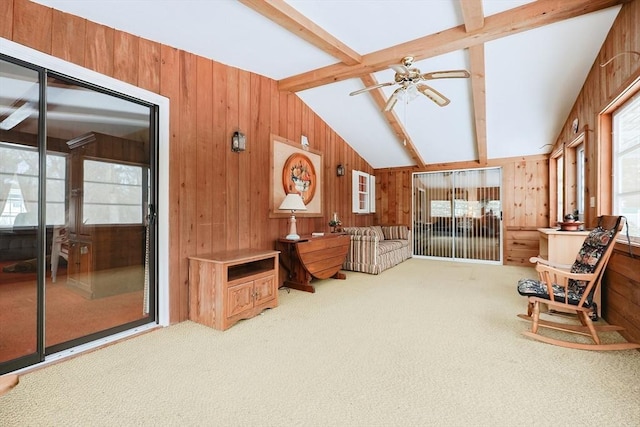 sitting room with carpet floors, wood walls, lofted ceiling with beams, and a ceiling fan