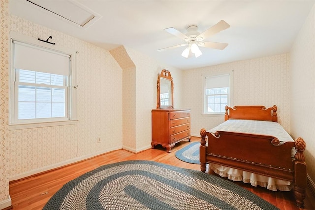 bedroom featuring wallpapered walls, attic access, baseboards, a ceiling fan, and wood finished floors