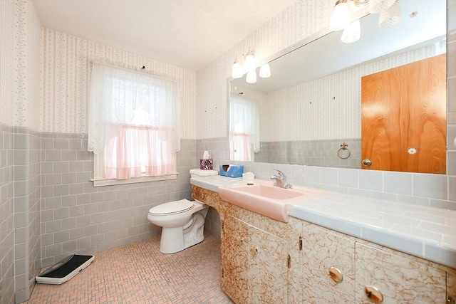 bathroom featuring tile walls, wallpapered walls, toilet, wainscoting, and tile patterned floors