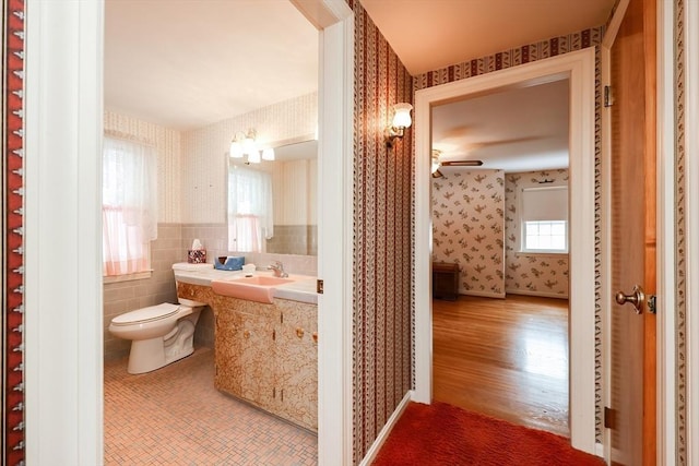 half bath with toilet, wallpapered walls, tile walls, and vanity