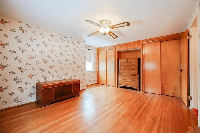 unfurnished bedroom featuring baseboards, light wood-style floors, multiple closets, and wallpapered walls