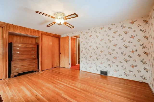 unfurnished bedroom with wallpapered walls, baseboards, visible vents, a ceiling fan, and wood finished floors