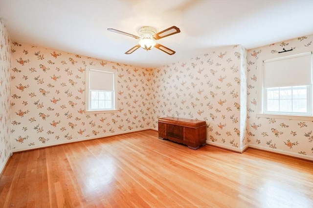 empty room with a ceiling fan, wood finished floors, baseboards, and wallpapered walls