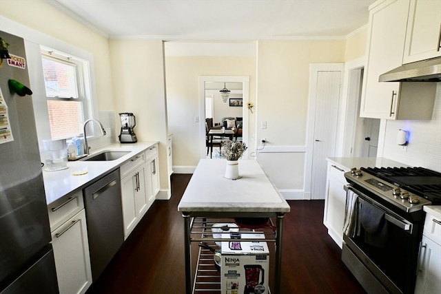 kitchen with stainless steel appliances, under cabinet range hood, a sink, dark wood-style flooring, and crown molding