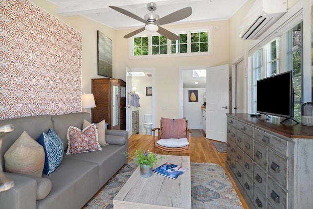 living room with a towering ceiling, a wall mounted AC, ceiling fan, and light hardwood / wood-style flooring