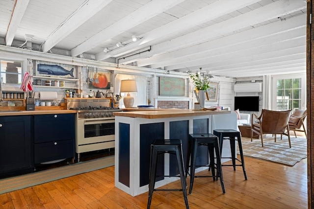 kitchen with stainless steel range, a kitchen breakfast bar, beam ceiling, and light hardwood / wood-style flooring