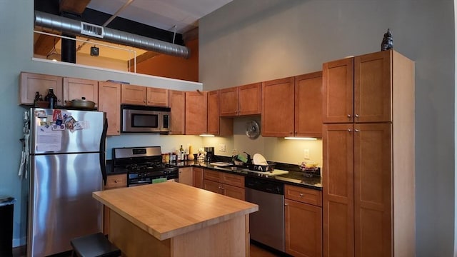 kitchen featuring visible vents, brown cabinets, a kitchen island, a high ceiling, and appliances with stainless steel finishes