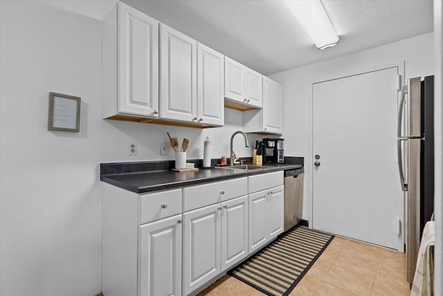 kitchen featuring sink, light tile patterned flooring, a textured ceiling, white cabinets, and appliances with stainless steel finishes