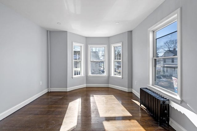 empty room with dark wood-type flooring, a wealth of natural light, and radiator