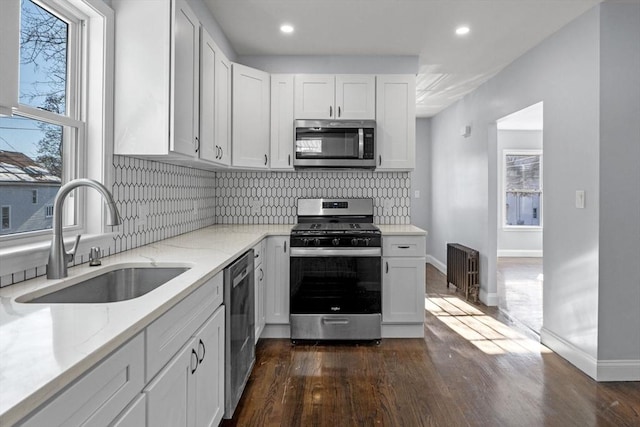 kitchen with white cabinets, appliances with stainless steel finishes, radiator heating unit, and sink