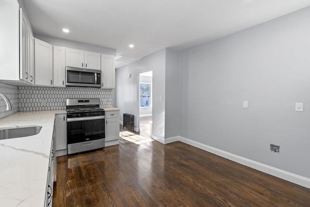 kitchen featuring light stone countertops, backsplash, white cabinets, appliances with stainless steel finishes, and sink