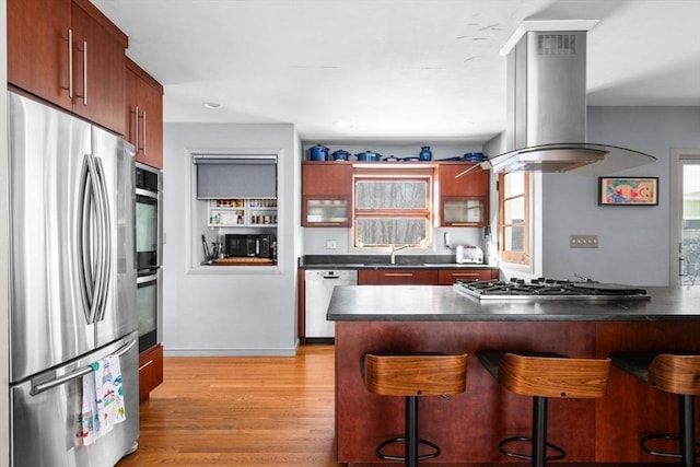 kitchen featuring a kitchen bar, sink, island range hood, light hardwood / wood-style flooring, and appliances with stainless steel finishes