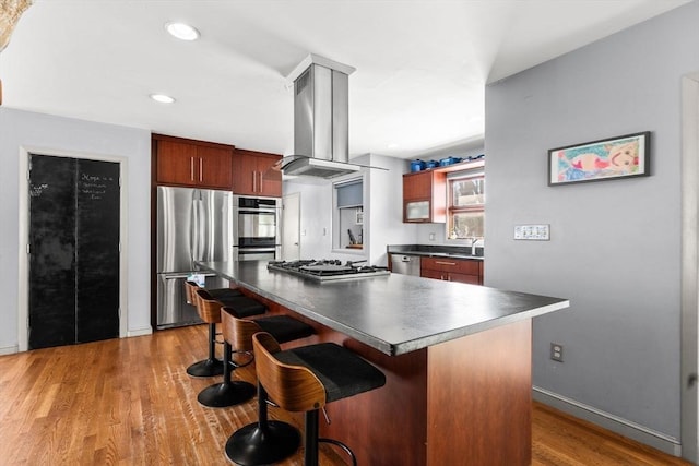 kitchen with a kitchen bar, island range hood, appliances with stainless steel finishes, a kitchen island, and hardwood / wood-style flooring