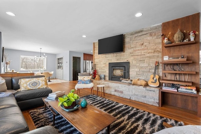 living room with hardwood / wood-style flooring, a stone fireplace, and a chandelier