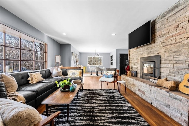 living room featuring wood-type flooring, a stone fireplace, and an inviting chandelier