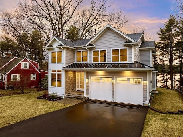 traditional home with an attached garage, driveway, a front yard, and a standing seam roof