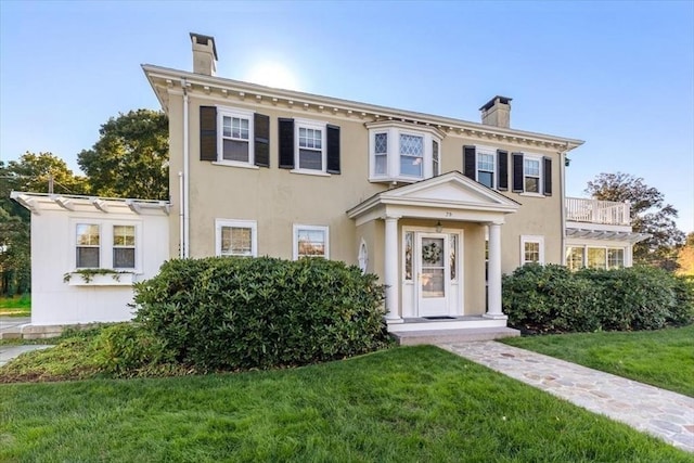 italianate home featuring a chimney, a front lawn, and stucco siding