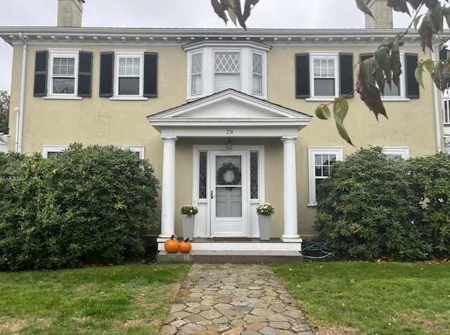 property entrance with a chimney, a lawn, and stucco siding