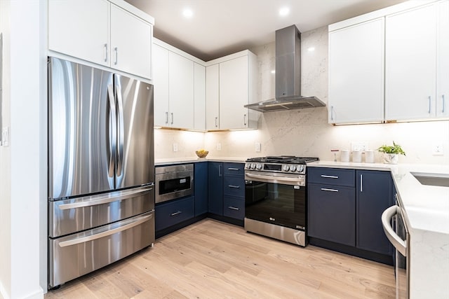 kitchen featuring stainless steel appliances, blue cabinets, wall chimney range hood, white cabinets, and light hardwood / wood-style floors