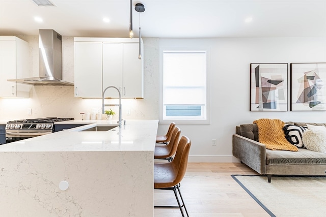 kitchen with wall chimney exhaust hood, sink, decorative light fixtures, white cabinetry, and stainless steel range with gas stovetop