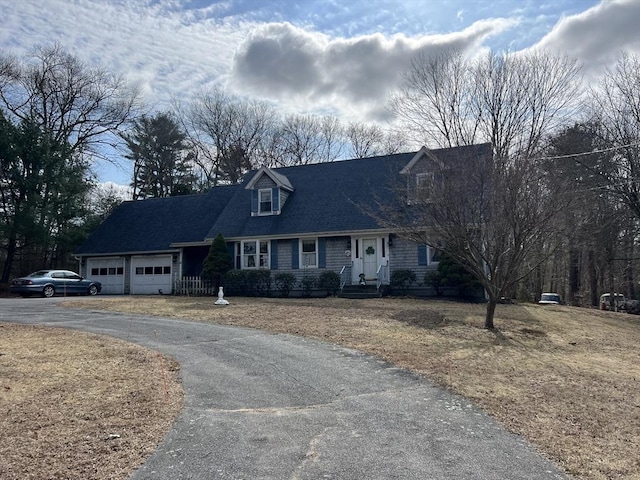 new england style home with aphalt driveway, an attached garage, and a shingled roof