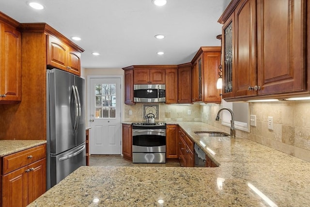 kitchen with a sink, stainless steel appliances, light stone counters, and decorative backsplash