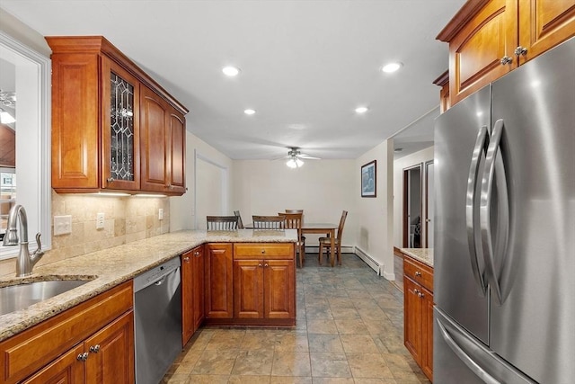 kitchen featuring tasteful backsplash, light stone countertops, a peninsula, stainless steel appliances, and a sink