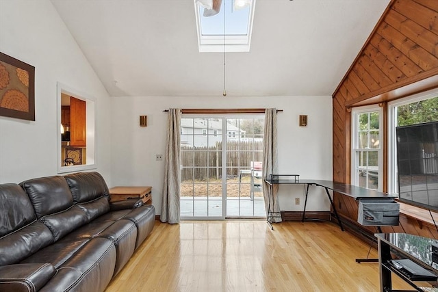 living room with baseboards, vaulted ceiling with skylight, and light wood finished floors